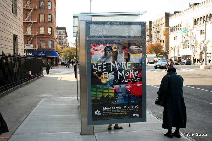 Гарлем. Чёрная старушка на автобусной остановке.
Надпись на рекламе: видь больше — будь больше. Нью-Йорк, CША