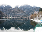Зимой озеро Рица помелело. Поверхность воды особенно спокойна и как зеркало отражает окружающие заснеженные горные хребты