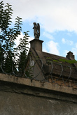 Высокие монументы со святыми и крестами наверху видно через высокий забор с колючей проволокой под напряжением.