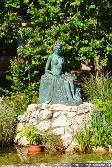 Скульптура Фея озера работы Йено Молнара установлена в 2000 году напротив западного входа. Девушка с гербом города, слева от нее — также херувим. Хевиз, Венгрия
