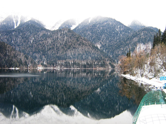 Зимой озеро Рица помелело. Поверхность воды особенно спокойна и как зеркало отражает окружающие заснеженные горные хребты Рица Реликтовый Национальный Парк, Абхазия