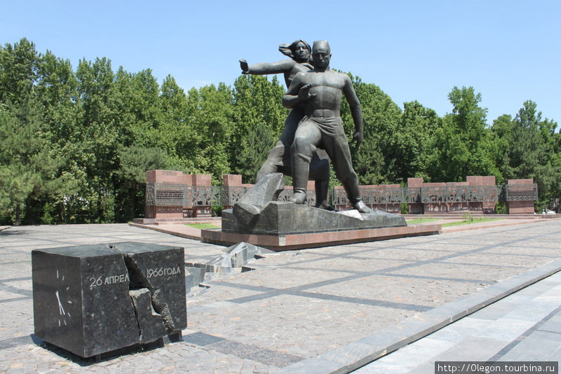 За кубом просечена трещина в земле, ведущая к бронзовой скульптуре, на которой изображены женщина с ребёнком на руках и впереди них мужчина, закрывший их собой от страшной стихии Ташкент, Узбекистан