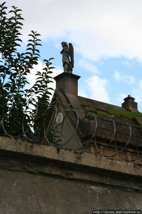 Высокие монументы со святыми и крестами наверху видно через высокий забор с колючей проволокой под напряжением. Сан-Паулу, Бразилия