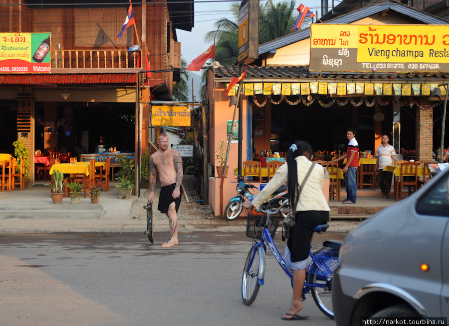 Готовый после тубинга турист, катается, хватаясь за проезжающие машины на скейте. Ванвьенг, Лаос